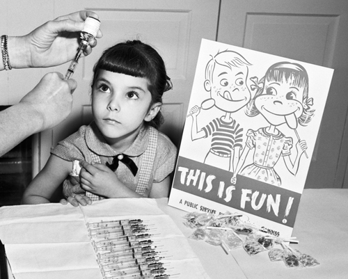 1950s girl watching nurse readying an immunization needle, sign beside says 'this is fun!'