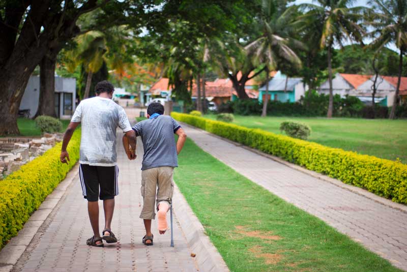 Man helping injured friend to walk through courtyard