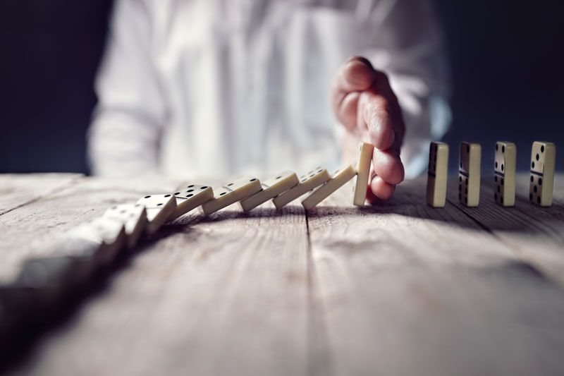 Row of dominoes falling, with man's hand stopping it from continuing
